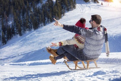 young couple sledding and enjoying on sunny winter day