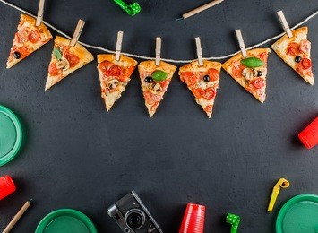 slices of pizza in the form of a garland with the attributes of a party. pizza slices on a gray concrete background. space for text. pizza menu. birthday with fast food.