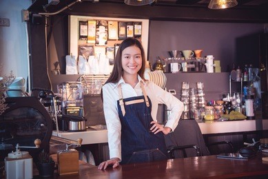 beautiful asian barista wearing apron ,standing and smiles in her cafe