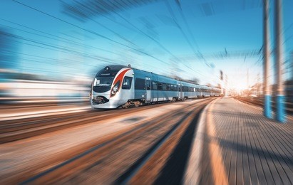 high speed train in motion at the railway station at sunset in europe. modern intercity train on railway platform with motion blur effect. industrial landscape. passenger train on railroad. vintage