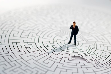 miniature people: businessman standing on center of maze. concepts of finding a solution, problem solving and challenge.