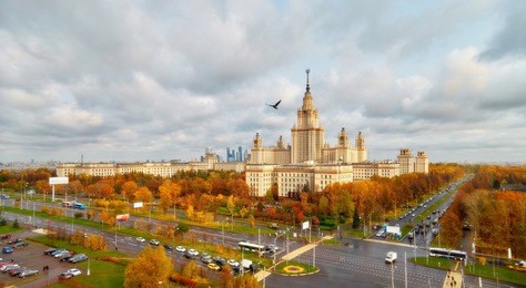 orton effect view of sunset orange color building of moscow university with glowing reflecting windows, red autumn trees, avenue crossing and heavy lead dramatic sky