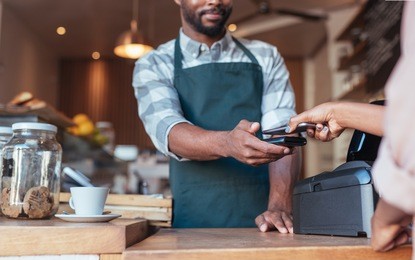 closeup of a barista using nfs technology to help a customer pay for a purchase with their smartphone in a cafe 