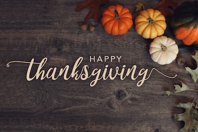 happy thanksgiving text with pumpkins and leaves over dark wood background