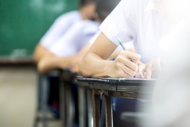 soft focus.high school or university student holding pencil writing on paper answer sheet.sitting on lecture chair taking final exam attending in examination room or classroom.student in uniform.