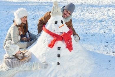 parents and child build snowman in winter as a family