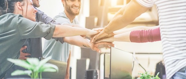 young team putting hands up for new startup in creative office - cheerful people giving strength motivation - soft focus on woman with red pullover hand - co-working and teamwork concept