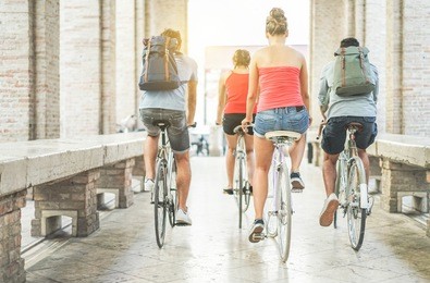 happy friends riding city bikes in old town center - young students having fun together going around with bicycles - youth, friendship and lifestyle concept - focus on right woman body 