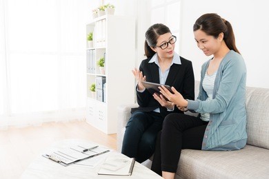 attractive young female insurance agent using mobile pad computer showing invest document for smiling girl and explaining plan.
