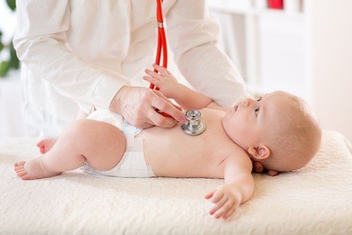 pediatrician examines baby boy using stethoscope to listen to baby's chest checking heart beat. child is looking at doctor