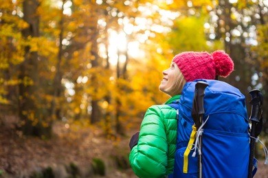 hiking woman with backpack looking at inspirational autumn golden forest. fitness travel and healthy lifestyle outdoors in fall season nature. female backpacker tourist walking and looking around.