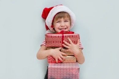 happy child in santa red hat holding christmas presents. christmas time.

