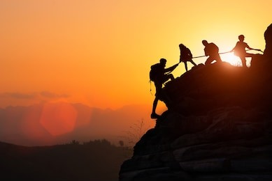 silhouette of the climbing team helping each other while climbing up in a sunset. the concept of aid. 