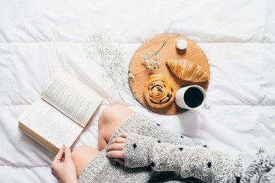 woman sitting in bed reading a book and having breakfast. top view 