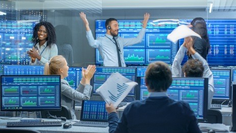 multi-ethnic team of traders have successful day at the stock exchange office. dealers and brokers buy and sell stocks on the market, they celebrate profitable transaction.