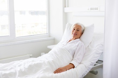 medicine, healthcare and old people concept - smiling senior woman lying on bed at hospital ward