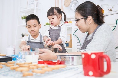 little asian girl with her brother and her mother baking cake and cookies in the kitchen. happy family and mother's day concept