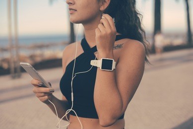 beautiful fitness woman hold hand wearing using smart watch phone, park outdoors background. tracking fitness application technology, listen music. healthy joyful sporty lifestyle. closeup portrait