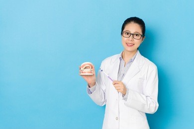 beautiful young female dentist showing teeth healthcare isolated on blue background.