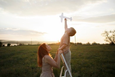 little boy and mother on the field in evening sunlight dreaming to fly like a plane.