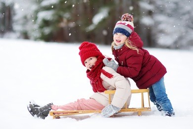 two funny little girls having fun with a sleight in beautiful winter park. cute children playing in a snow. winter activities for kids.