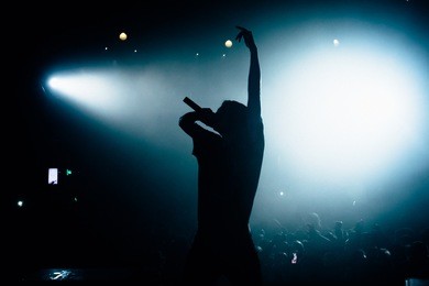 silhouette of singer rising his hand opposite stage crowd. floodlights lightning at the camera. beautiful pool of white light on the background.