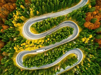 aerial view of lorry winding up its way on a curvy road through autumn colored forest