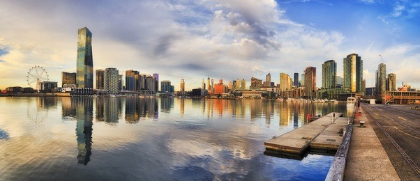 new high-rises of melbourne in docklands suburb reflecting in still waters of yarra river from amusement wheel to concrete pier with marina in between.