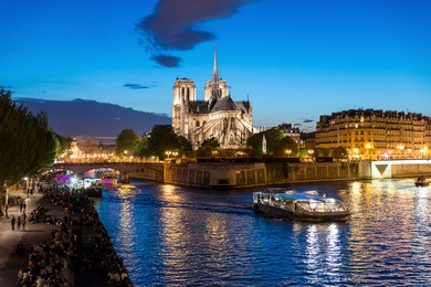 notre dame de paris with cruise ship on seine river at night in paris, france