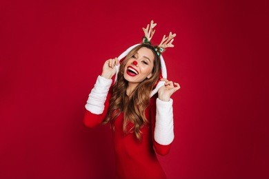 image of cheerful young woman wearing christmas deer costume standing isolated over burgundy background wall. looking at camera.