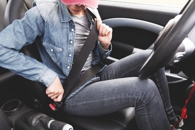 a hipster girl wearing jeans clothes fastens her seat belt in the car.