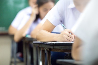 soft focus.high school or university student holding pencil writing on paper answer sheet.sitting on lecture chair taking final exam attending in examination room or classroom.