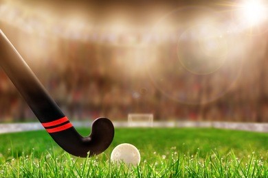 low angle view of field hockey stick and ball on grass and deliberate shallow depth of field on brightly lit stadium background with lens flare and copy space.