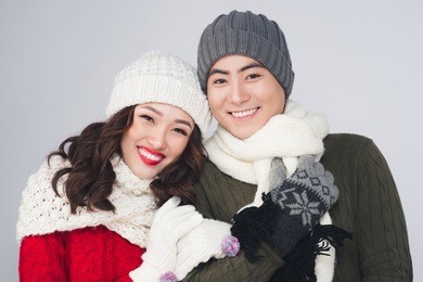 smiling young asian couple wearing knitted warm scarf, over gray background