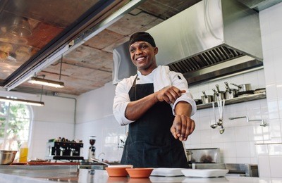 happy male cook wearing apron standing by kitchen counter and smiling. gourmet chef in uniform at restaurant kitchen.