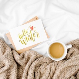 hello winter postcard and cup of coffee on bed with warm plaid. copy space. flat lay, top view