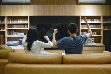 asian couple cheering in front of tv in living room at night