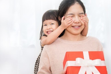 little asian girl surprise her mother with gift box her hands cover her mother face. boxing day holiday birthday christmas and mother's  day concept.