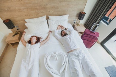 happy couple in luxury hotel room, holidays travel accommodation, top view of smiling man and woman lying down on the bed