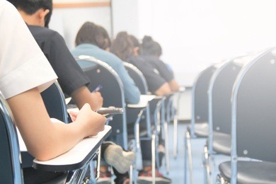 hands university student holding pen writing /calculator doing examination / study or quiz, test from teacher or in large lecture room, students in uniform attending exam classroom educational school.