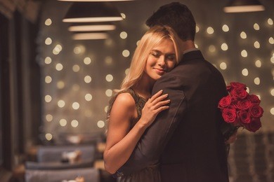 beautiful girl is holding roses and smiling while hugging her boyfriend during their date in restaurant