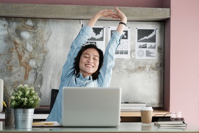asian businesswoman stretching body for relaxing while working with laptop computer at her desk, office lifestyle, business situation, working at home