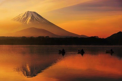 mt. fuji or fujisan with silhouette three fishing people on boats and mist at shoji lake with twilight sky at sunrise in yamanashi, japan. landscape with beautiful skyline reflection on the water.