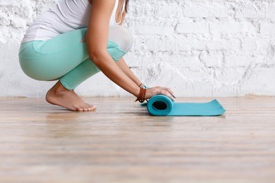 close-up of attractive young woman folding blue yoga or fitness mat after working out at home in living room. healthy life, keep fit concepts. horizontal shot. white loft studio
