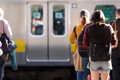 young japanese woman wearing shorts and carrying a black backpack hunched over her phone while while waiting for her train in a railway station in tokyo.