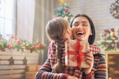 merry christmas and happy holidays! cheerful mom and her cute daughter girl exchanging gifts. parent and little child having fun near tree indoors. loving family with presents in room.