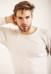 young fashion man in white t-shirt posing near white wall and looking at camera with hand