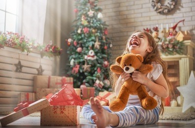 happy holidays! cute little child opening present near christmas tree. the girl laughing and enjoying the gift. 