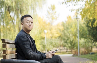 asian middle-aged men in the autumn park, watching cell phones, smiling