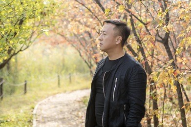 the middle-aged asian man smiles on the park road in autumn